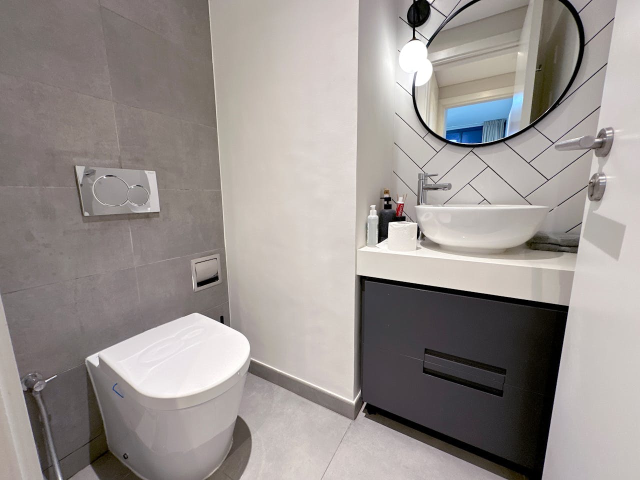 A contemporary bathroom featuring sleek design elements, round mirror, and modern fixtures.